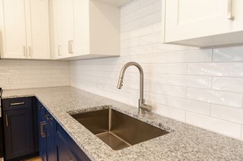 A kitchen with a sink and a white tile backsplash at The Crest at Oakwood Apartments, Georgia
